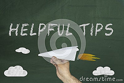 Hand holding paper plane and Text Helpful Tips written on green blackboard Stock Photo