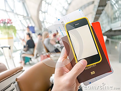 Hand holding passport, boarding pass and smart phone in airport Stock Photo