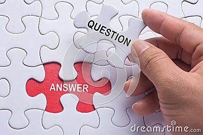 Hand holding piece of jigsaw puzzle with word question & answer. Stock Photo