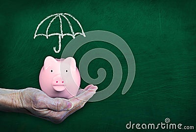 Saving For Rainy Day With Hand Holding Piggy Bank on Chalkboard Background Stock Photo