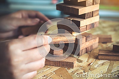 A hand holding and playing Jenga or Tumble tower wooden block game Stock Photo