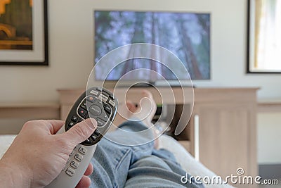 Hand Holding remote Control for TV while relaxing with feet propped up - Shallow depth of field Stock Photo