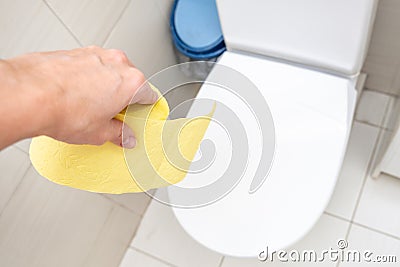 A hand holding a roll of yellow toilet paper in a lavatory, restroom, digestive problems concept Stock Photo