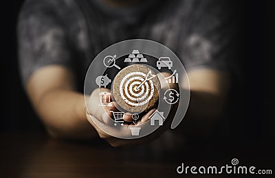 Hand holding round wooden with white dartboard and business icon include gold bar , car , dollar ,house and piggy saving for setup Stock Photo