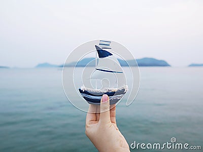 Hand holding sailboat model over blue sea Stock Photo