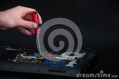 Hand holding a screwdriver repairing an opened laptop on dark background Stock Photo