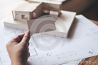 A hand holding and showing an empty business card with an architecture model and shop drawing paper on table in office Stock Photo