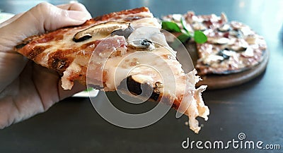 Hand holding a slice of Mushroom and Bacon Pizza Stock Photo