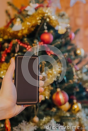 Smartphone in xmas. Hand showing a smartphone against Christmas tree at home Stock Photo