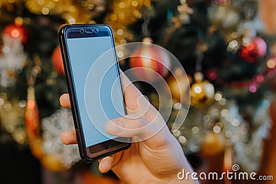 Smartphone in xmas. Hand showing a smartphone against Christmas tree at home Stock Photo