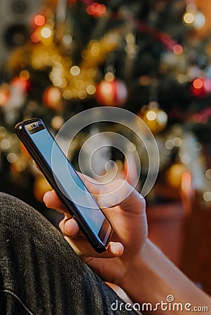 Smartphone in xmas. Hand showing a smartphone against Christmas tree at home Stock Photo