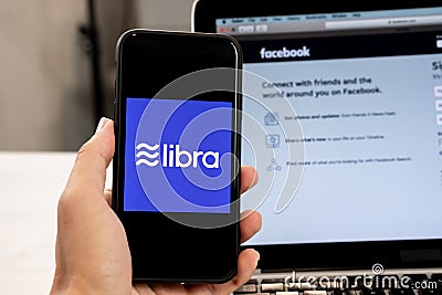 18 June 2019, Ljubljana Slovenia - Hand holding a smartphone with Libra logo on it, next to Facebook website opened on Editorial Stock Photo