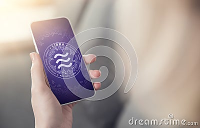 Hand holding smartphone with Libra symbol on screen. New era in e-commerce, on-line payments and e-business concept. New virtual Editorial Stock Photo