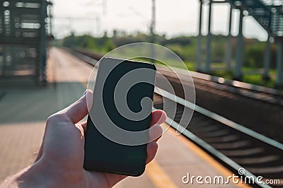 Hand holding a smartphone with railway station in the background Stock Photo