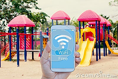 Hand holding smartphone with WiFi Free on screen over outdoor play park blurred Stock Photo