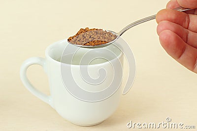 Hand holding a spoon with instant coffee over coffee cup Stock Photo