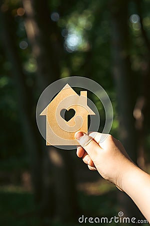 Hand holding a sunlit wooden house model against a forest background. Stock Photo