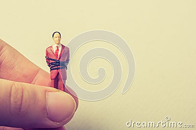 Hand holding tiny figurine of man model tied in rope Stock Photo