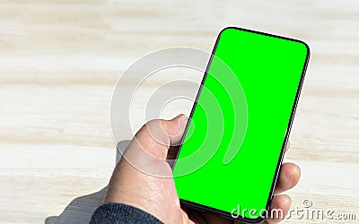 Hand holding upright black smartphone with chrome green screen on a light wooden table Stock Photo