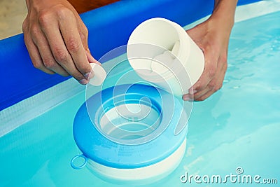 Hand holding white chlorine tablets over swimming pool skimmer. Chlorination of water in pool for disinfection and Stock Photo