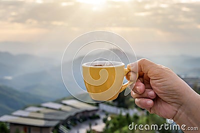 Hand holding a white cup of hot espresso coffee mugs and nature view of the mountain landscape in the morning with sunlight Stock Photo