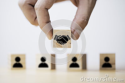 Hand holding wooden cube which drawing of hand shaking print screen on wooden cube block in front of human icon for business deal Stock Photo