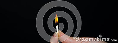 A hand holds a burning match on a black background. A wooden match burns in the hands of a macro. Igniting a match on a box. Smoke Stock Photo