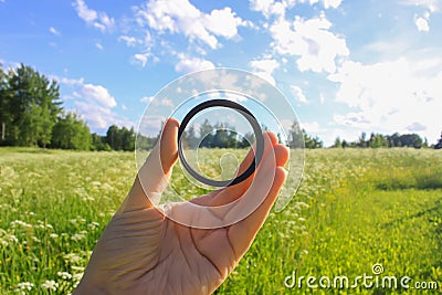 Hand holds a polarizer filter on summer landscape background. Stock Photo