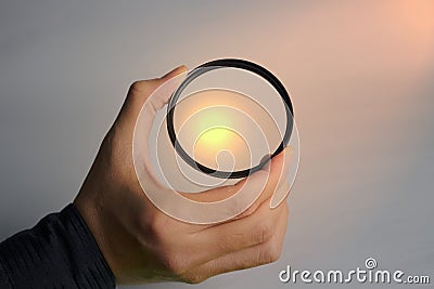 Hand holds clear lens camera filter on white background with light focus Stock Photo