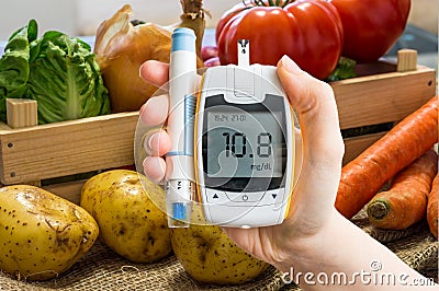 Hand holds glucometer for measuring glucose level. Vegetables in background. Stock Photo