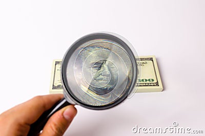 The hand holds a magnifying glass and looks at a bill of one hundred dollars. Focus the portrait of Franklin on the bill Stock Photo