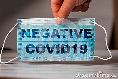 The hand holds a medical and protective mask with the word NEGATIVE TEST CORONAVIRUS. Concept of coronavirus quarantine. Prevent Stock Photo