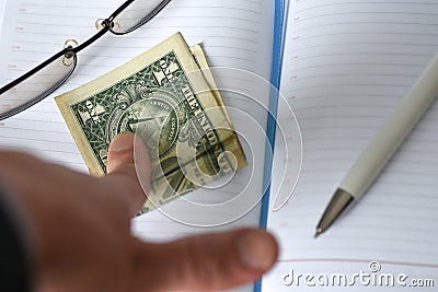 The hand holds the money in the notebook on the desk in the office. A bribe giving. corruption. Dollars for work. work done for mo Stock Photo