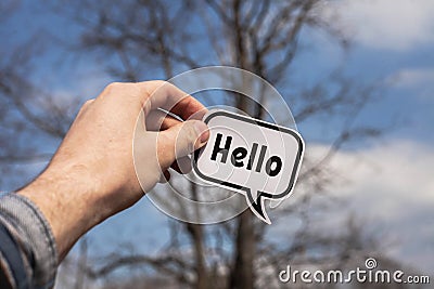 A hand holds a paper cloud with the word hello on the background of trees Stock Photo