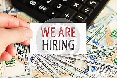 On the table are bills, a bundle of dollars and a sign on which it is written - WE ARE HIRING. Finance and economics concept Stock Photo