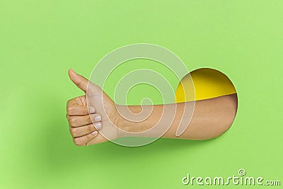 Hand through hole in green background keeps thumb up, demonstrates approval sign showing like gesture Stock Photo