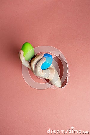 Hand in a hole of pink paper.Eggs painted for Easter. Trend. Blue, green on a pink background. Stock Photo