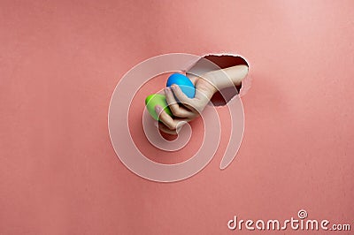 Hand in a hole of pink paper.Eggs painted for Easter. Trend. Blue, green on a pink background. Stock Photo