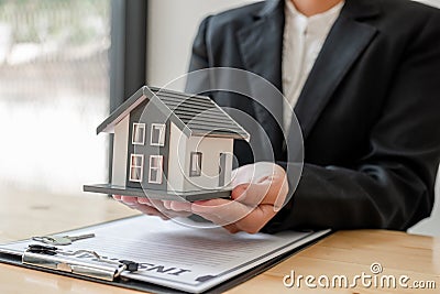 The hand of a home insurance agent is holding a modelhome to protect the safety for customers buyers Stock Photo