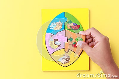 Hand of kid holding wooden jigsaw of the 5 food Groups. Child de Stock Photo