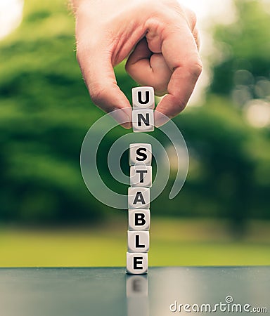 Hand lifts two dice and changes the word unstable to stable Stock Photo