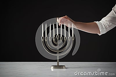 Hand Lighting Candle On Metal Hanukkah Menorah On Marble Surface Against Black Studio Background Stock Photo