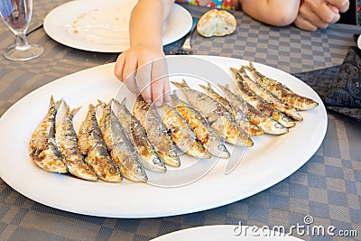 Hand of little child taking sardines in a row cooked in a big white dish Stock Photo