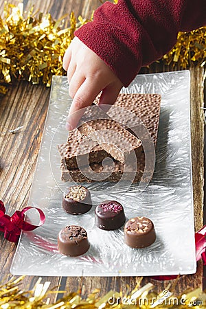 Hand of a little girl picking up a piece of chocolate nougat during the Christmas holidays. Stock Photo