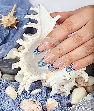 Hand with long artificial blue french manicured nails holding a seashell Stock Photo