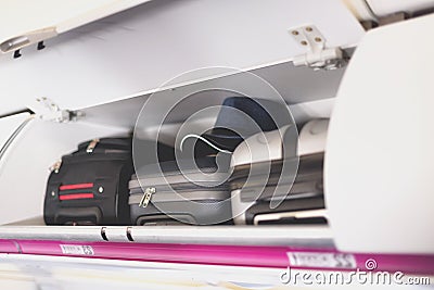 Hand-luggage compartment with suitcases in airplane. Carry-on luggage on top shelf of plane. Travel concept with copy Stock Photo