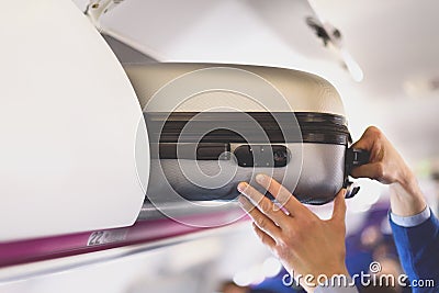 Hand-luggage compartment with suitcases in airplane. Hands take off hand luggage. Passenger put cabin bag cabin on the Stock Photo