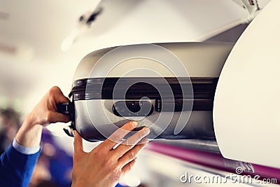 Hand-luggage compartment with suitcases in airplane. Hands take off hand luggage. Passenger put cabin bag cabin on the Stock Photo