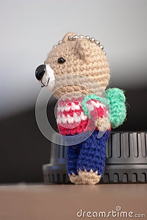 Hand made key ring brown teddy bear knitted doll wearing a red and white shirt and blue plant Stock Photo