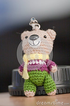 Hand made key ring brown teddy bear knitted doll wearing a violet and white shirt and green plant Stock Photo